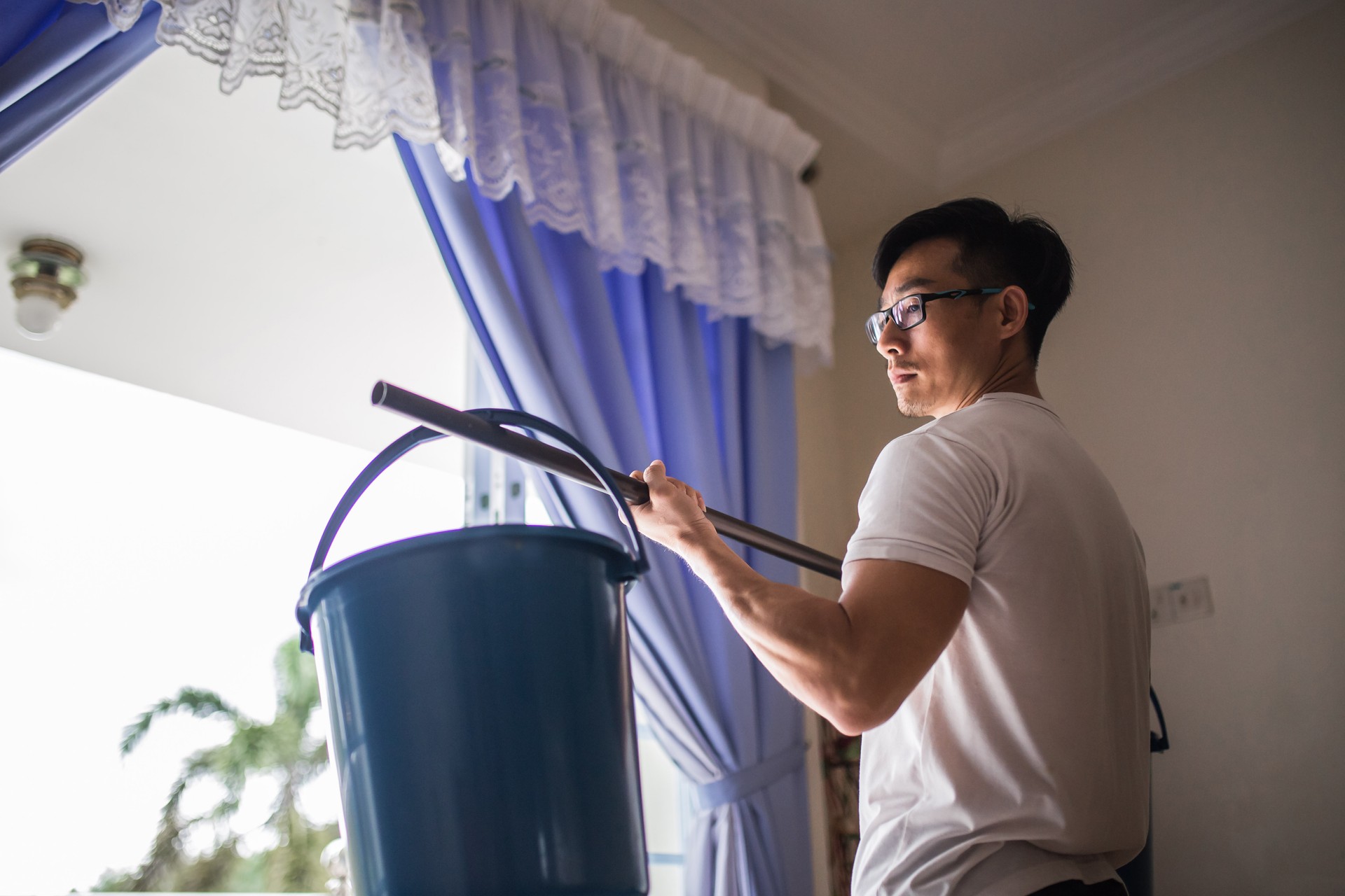 An Asia Chinese man lifting bucket instead of gym weights equipment training at home due to coronavirus Covid-19 pandemic lockdown issue.